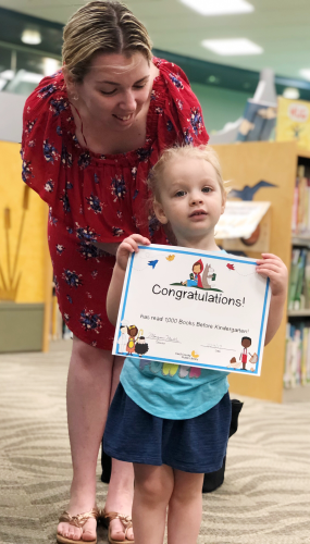 A young girl, pictured with her mother, holding her program completion certificate
