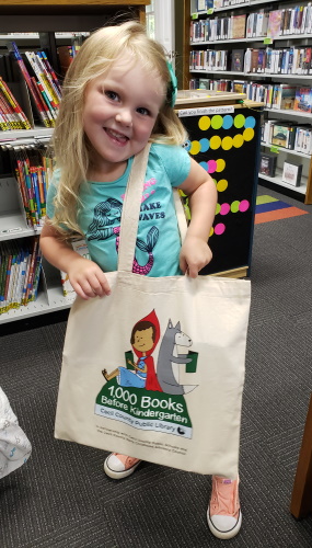A young girl holding her 1,000 books before kindergarten tote bag
