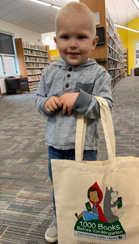 A young boy holding his 1,000 books before kindergarten tote bag